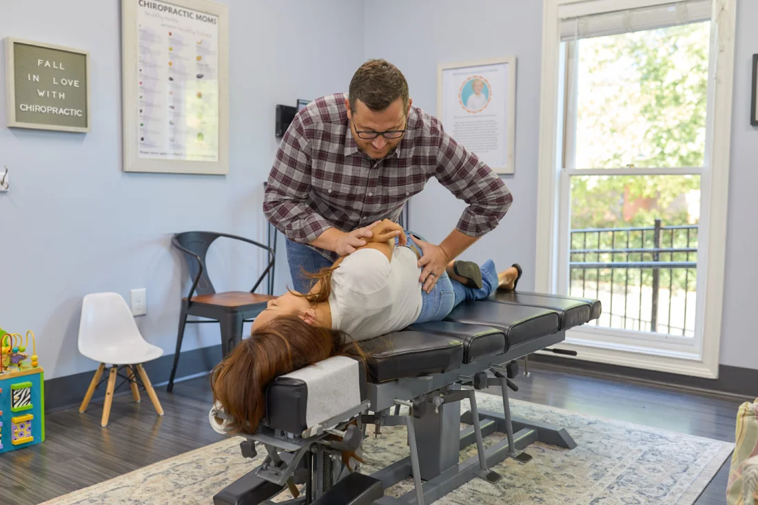 Male chiropractor performing adjustment on woman's back while she lays on treatment table