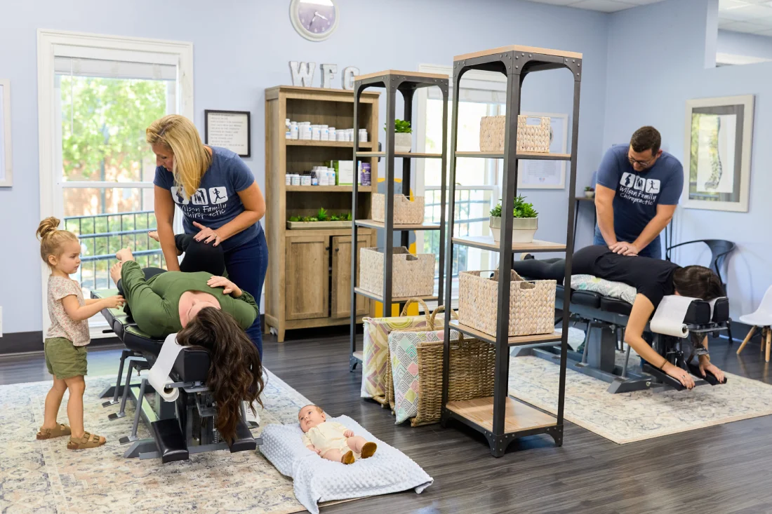 Tow chiropractors perform adjustments on members of a family while other family watch in the clinic