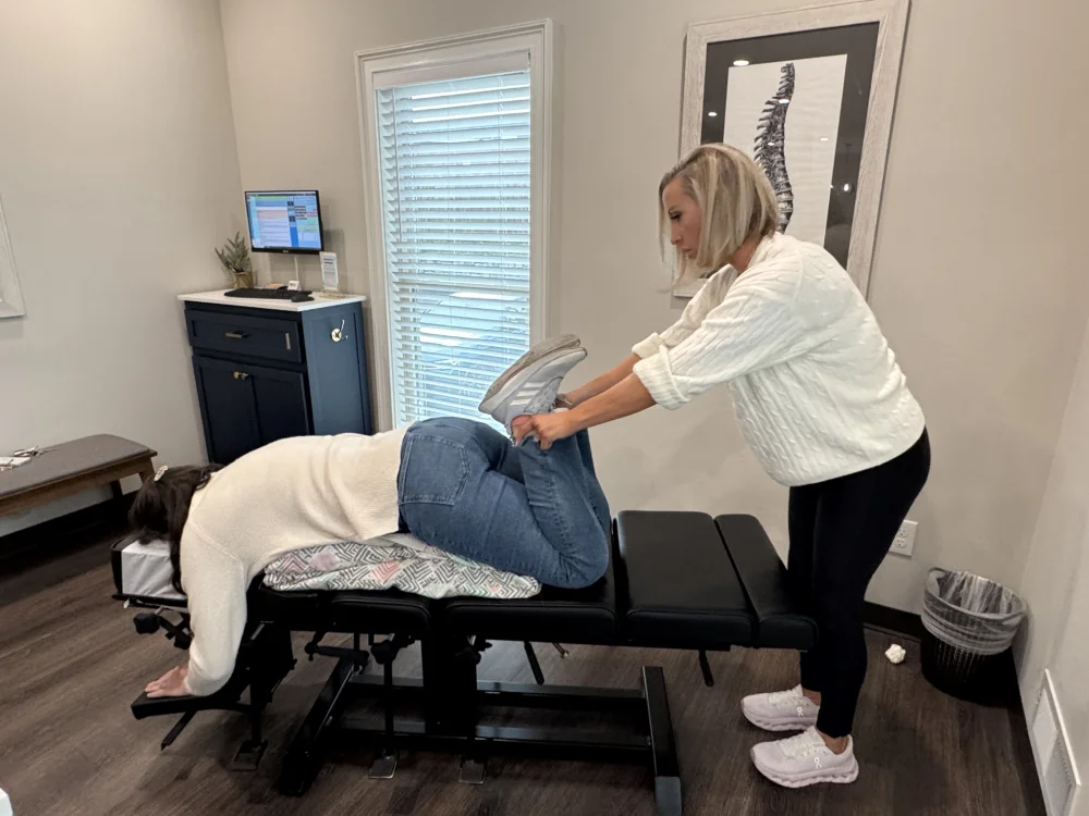 Female chiropractor hinges pregnant woman's legs at the knees while she lays face down on the treatment