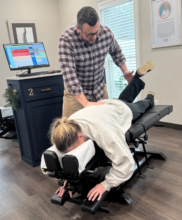 Male chiropractor performs assessment on female patient as she lays on treatment table