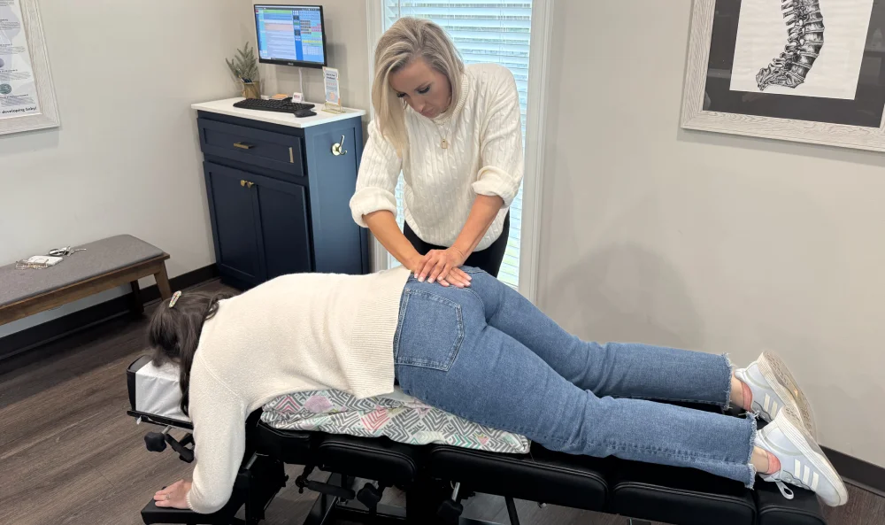 Female chiropractor performs adjustment on woman's low back while she lays on treatment table