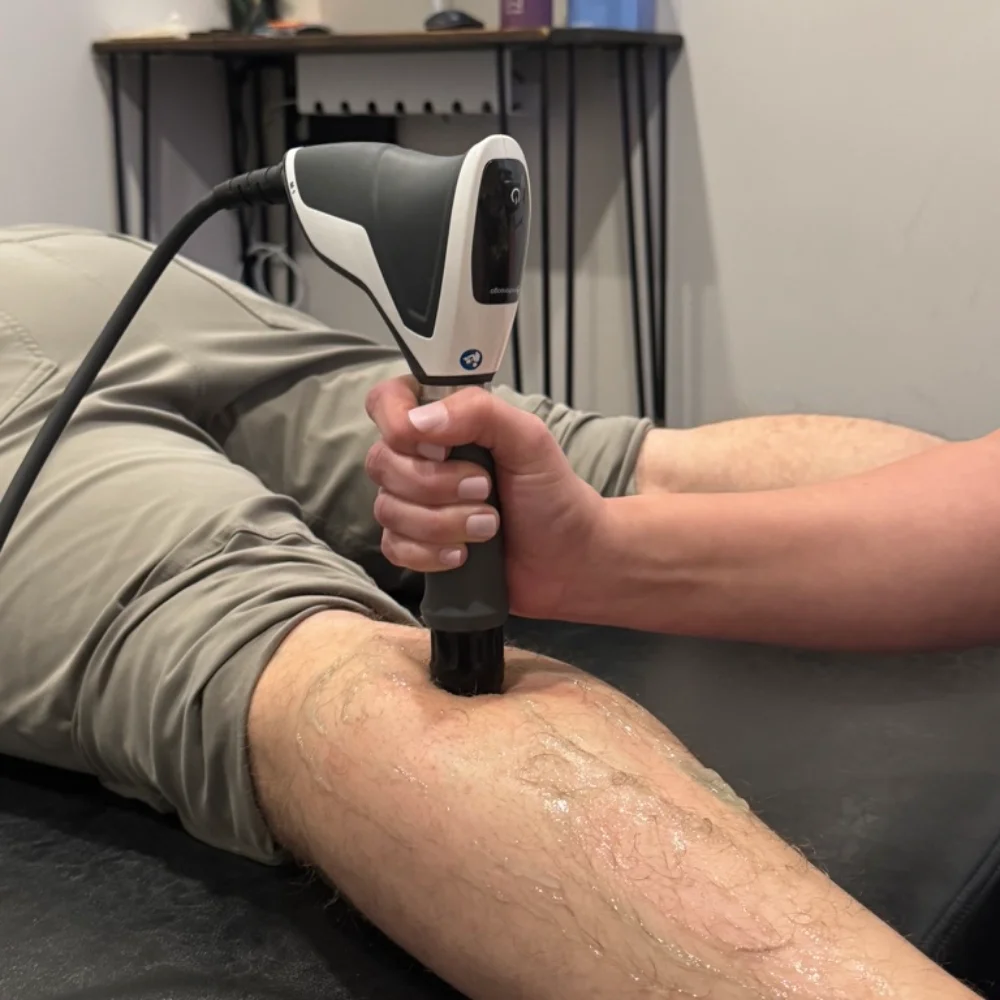 Male chiropractor administers treatment to woman's neck and shoulder muscles while she sits on treatment table